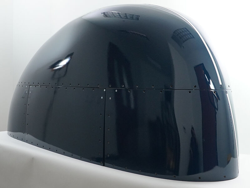 Multipart radome. This flight-qualified hardware is painted a glossy dark blue. It has a rounded shape and sits on a white table and background.