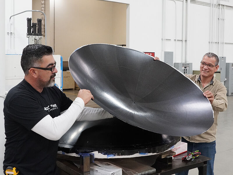 Carbon fiber reflector surface panel is released from the tool and held up by two technicians.