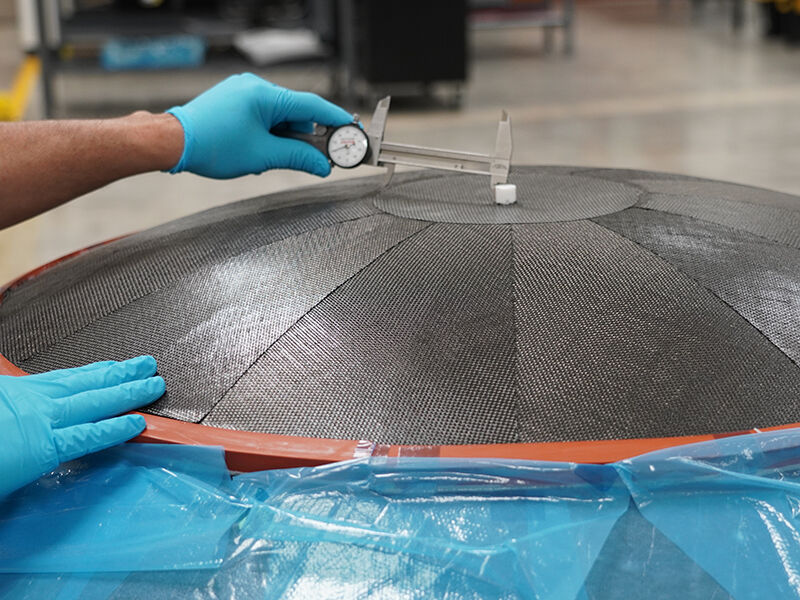 Carbon fiber reflector under manufacture. Pausing during the layup process, the technician is measuring from the center to the edge of the center circular panel to verify accuracy.