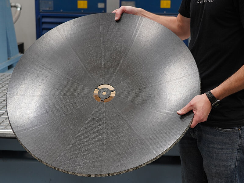 Technician holding up and displaying the dish of a carbon fiber reflector after being machining