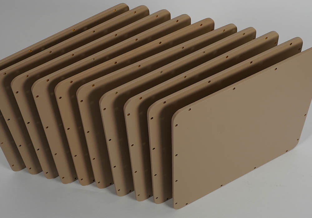 A grouping of radome covers that are rectangular in shape with rounded corners, painted a tan color, and machined with four attachment holes along each edge. Photographed on a neutral background.